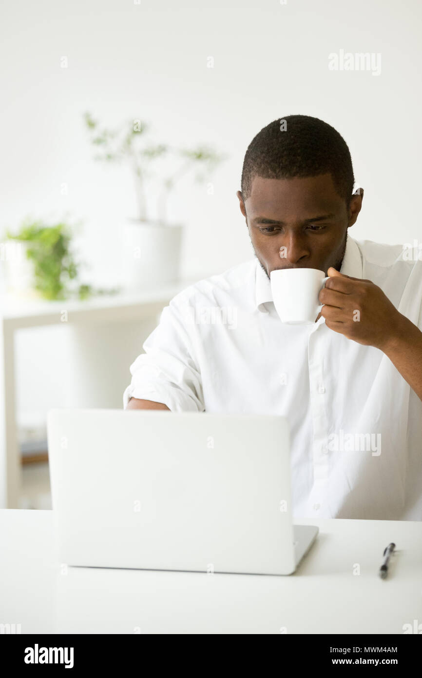Focused black worker drinking coffee checking emails in office Stock Photo