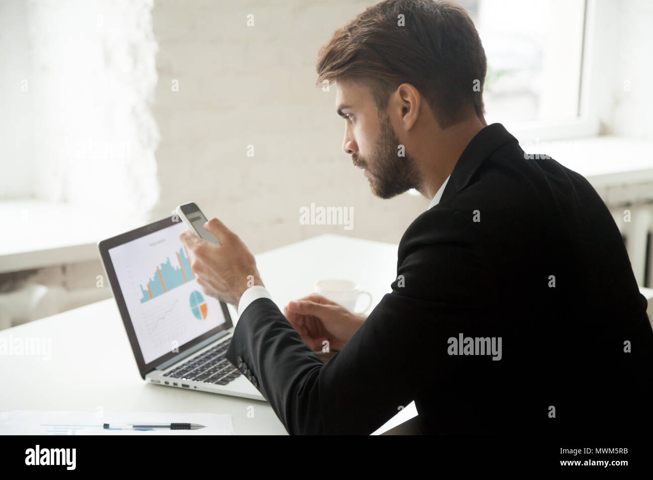 Serious entrepreneur writing email on cellphone while working at Stock Photo
