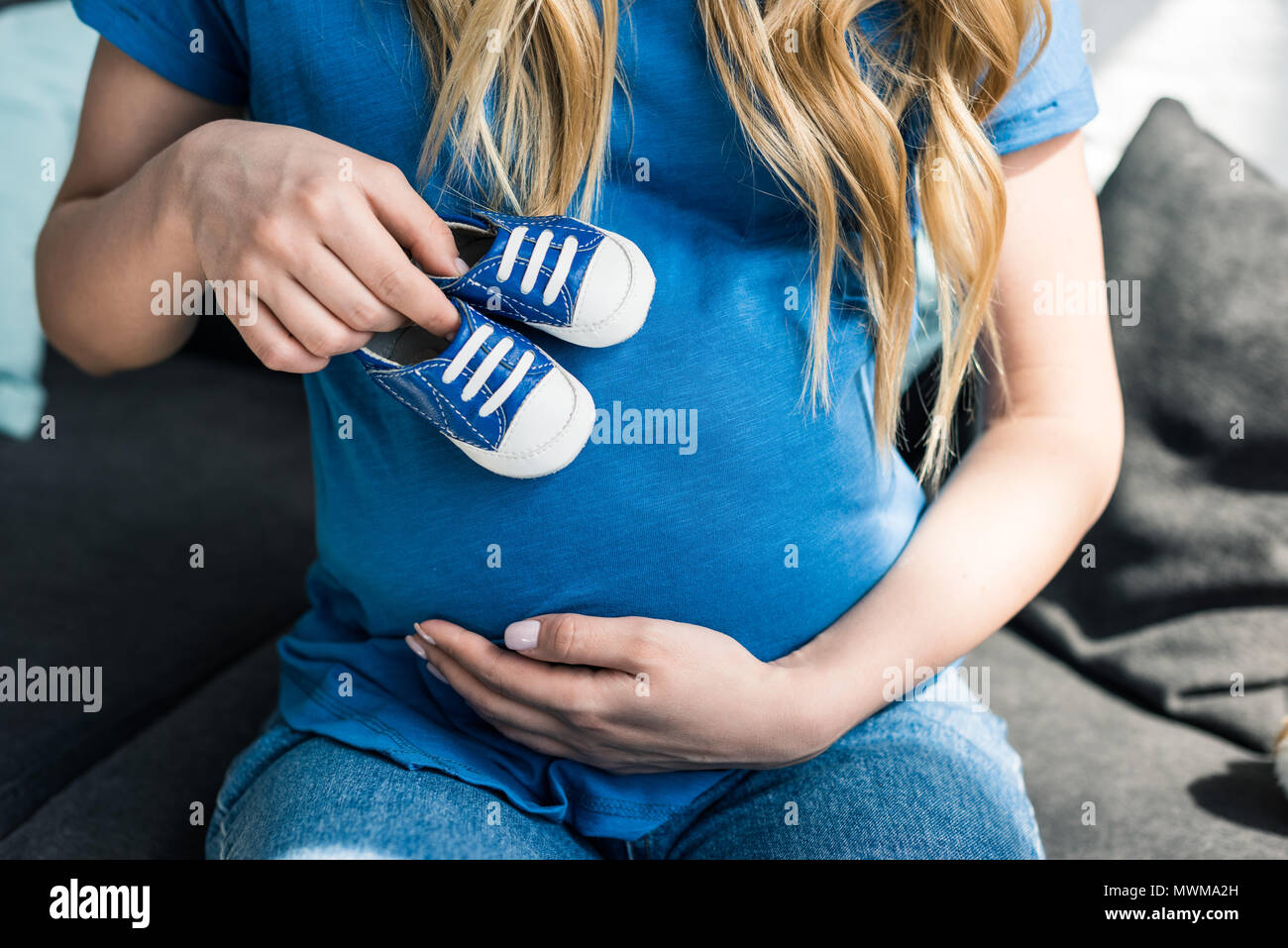 cropped image of pregnant woman touching belly with baby shoes Stock Photo