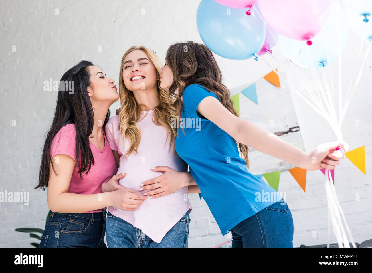multicultural friends kissing smiling pregnant woman at baby-party Stock Photo
