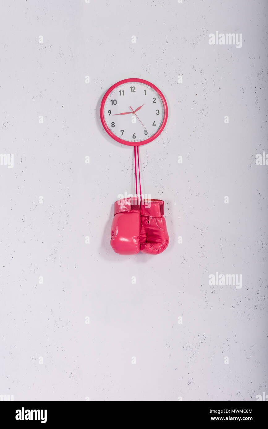 pink boxing gloves hanging at pink wall clock on white Stock Photo