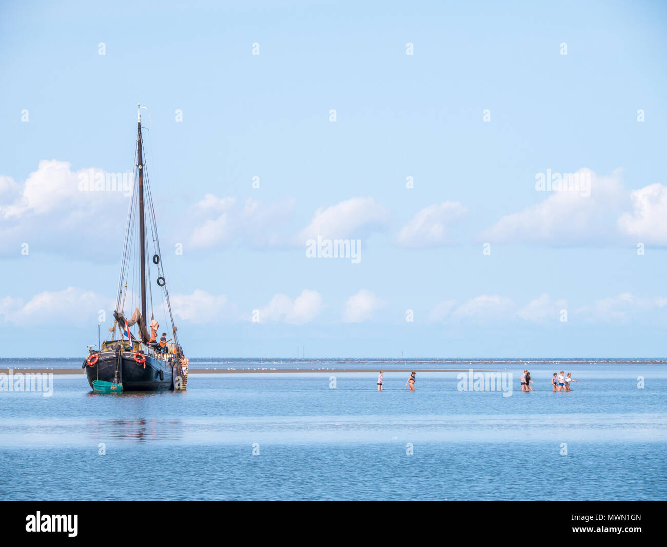 Group of youngsters wading in shallow water and sailing yacht aground at low tide on Wadden sea, Netherlands Stock Photo