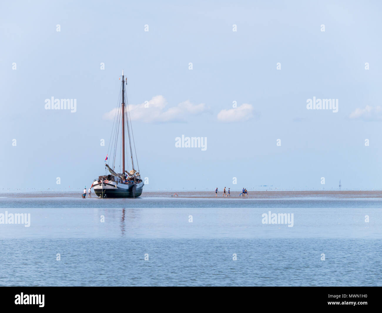 Group of youngsters playing on sand flat and dried out flat-bottom sailing yacht at low tide on Wadden sea, Netherlands Stock Photo