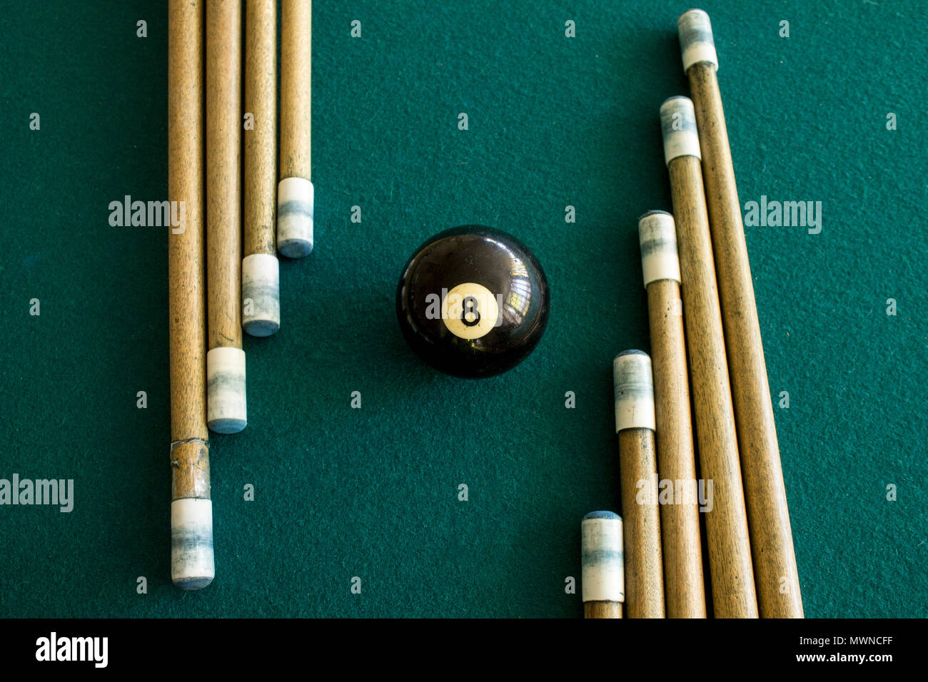 Eight ball billiard in the middle of a group of cues on a green table Stock Photo