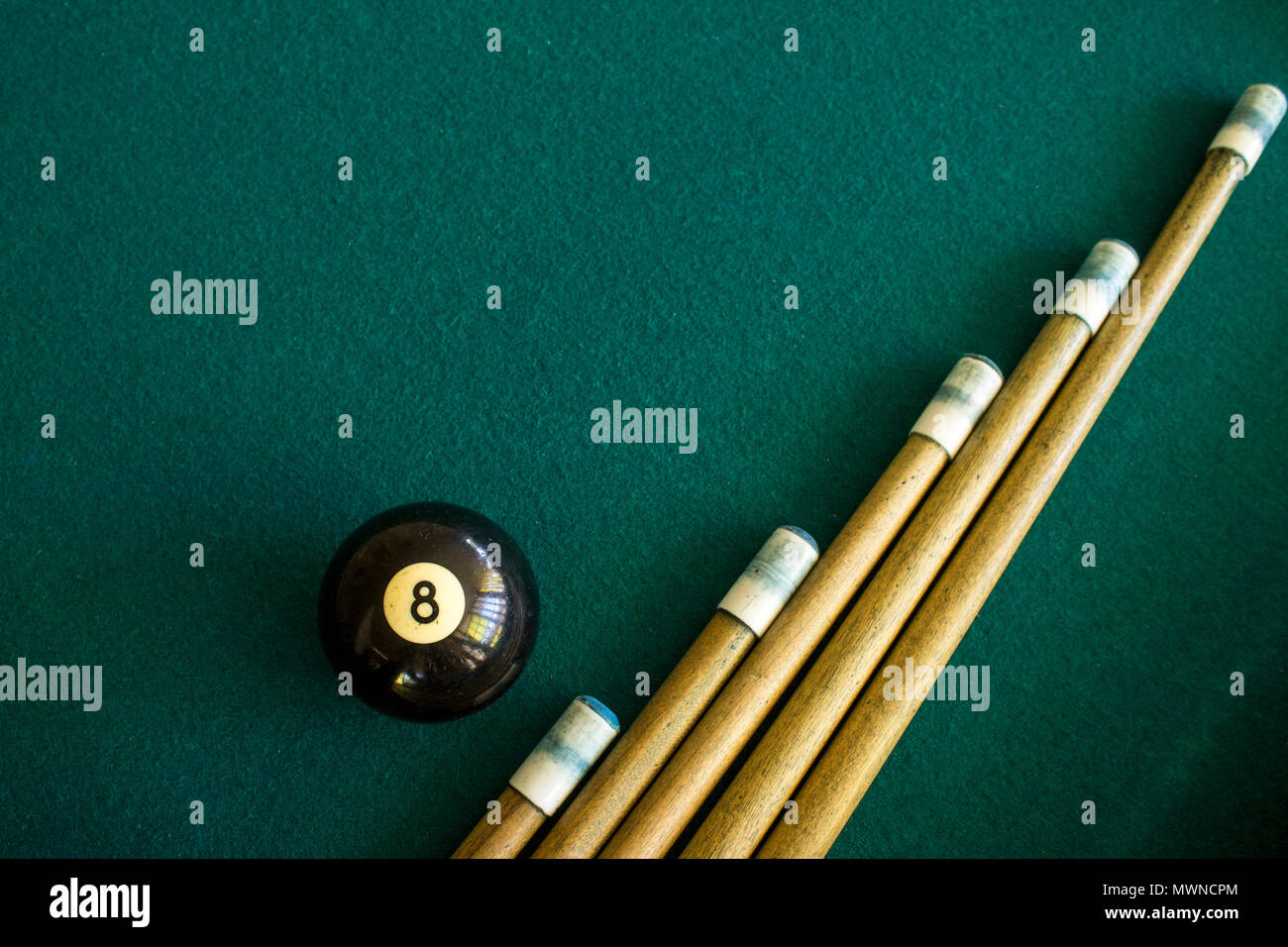 Eight black billiard ball on a green billiard table next to a group of a cue sticks Stock Photo