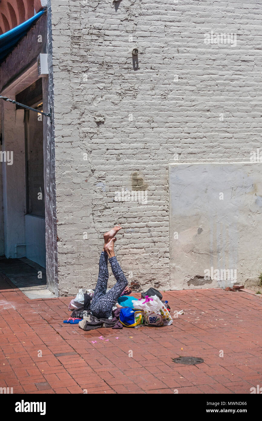 An Older Adult Female Homeless Person Lies On The City Sidewalk And Stretches Her Legs Stock