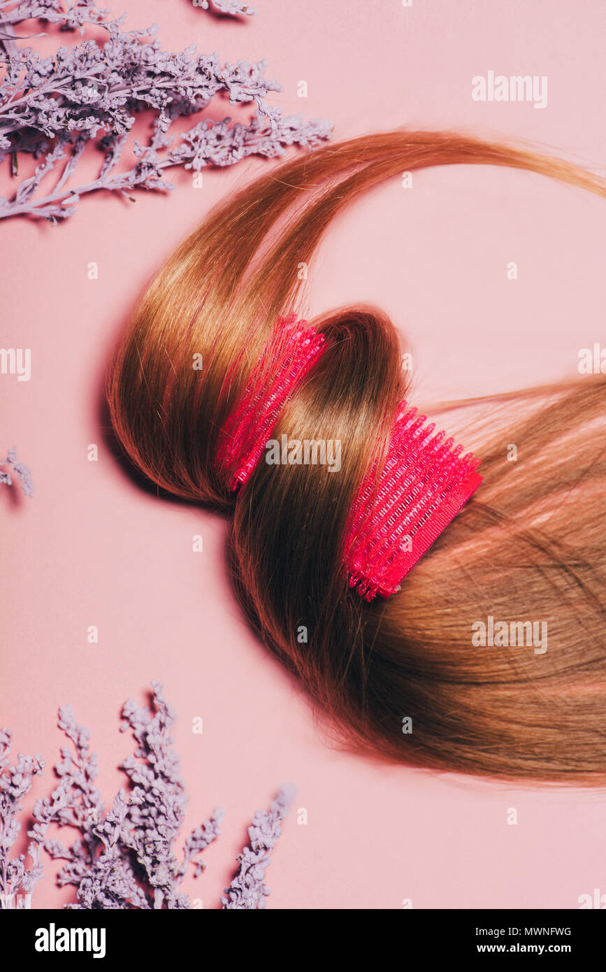 top view of hair rolled over curler with flowers on pink surface Stock
