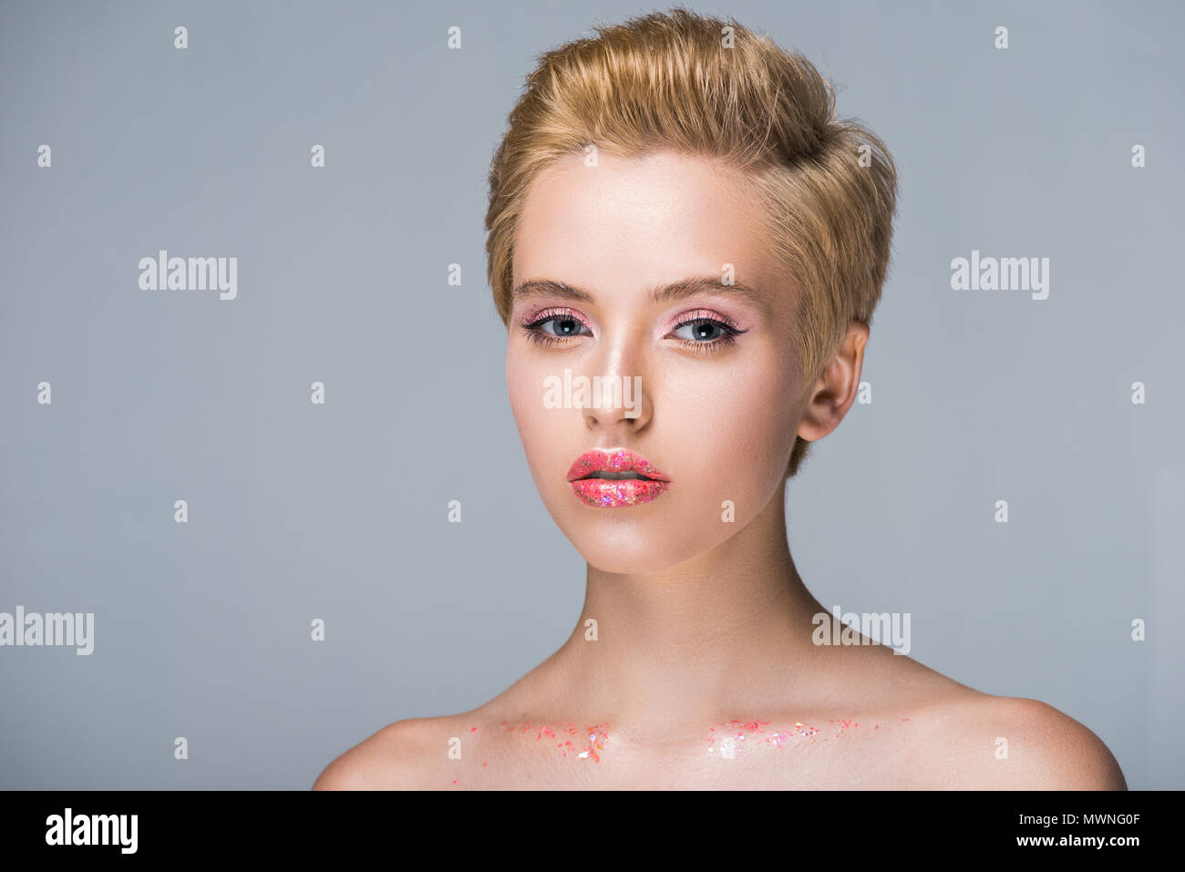 attractive woman with glitter on face and body looking at camera isolated on grey Stock Photo
