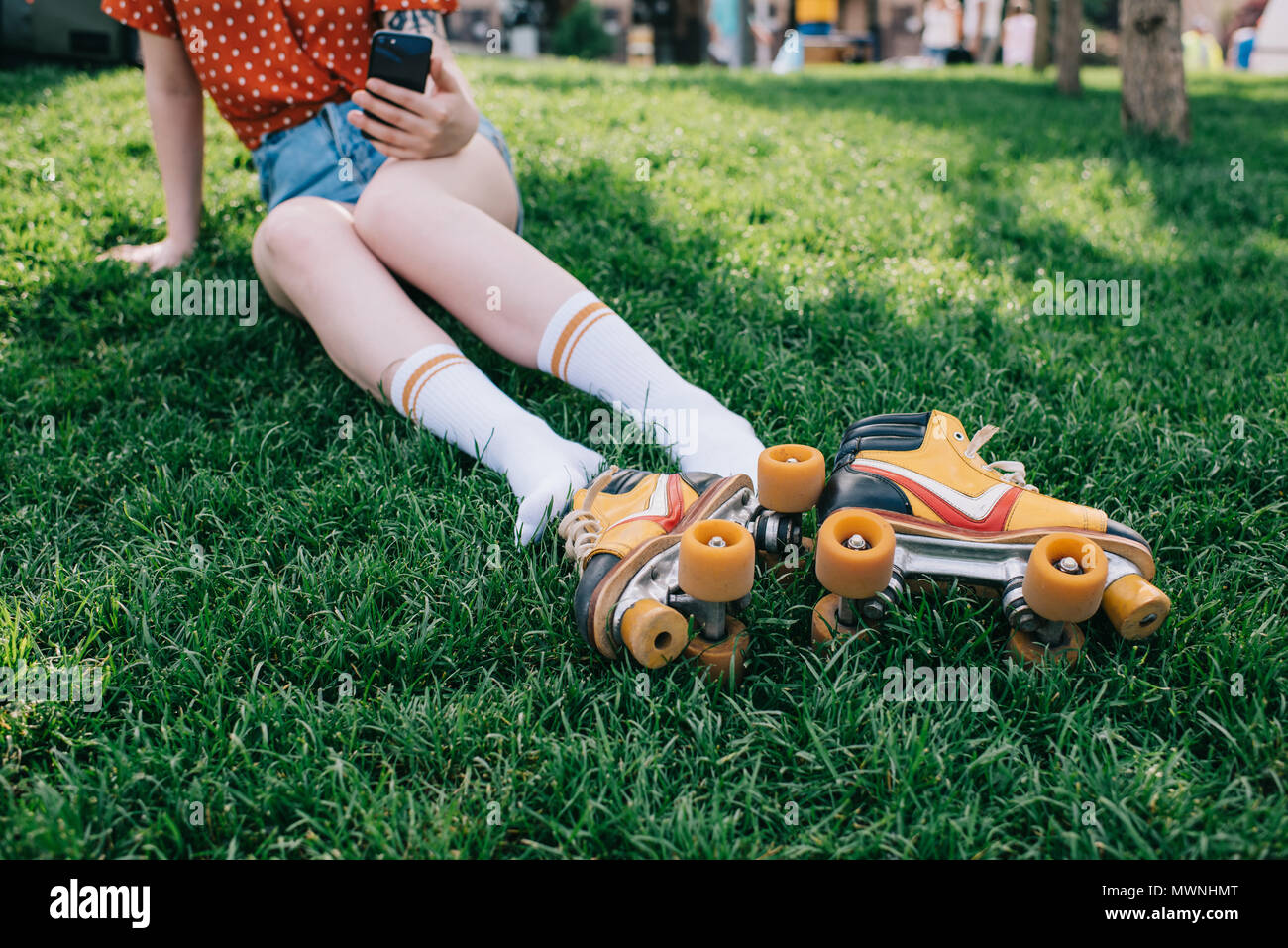 cropped shot of girl in socks using smartphone while resting on grass with roller skates Stock Photo