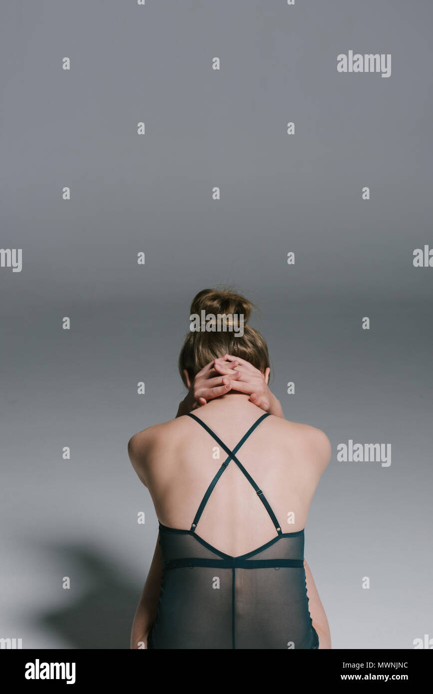 back view of woman with slim body wearing swimsuit and sitting on grey Stock Photo