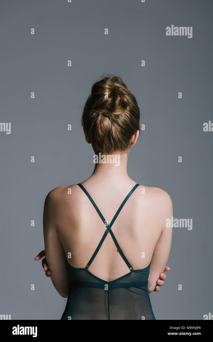 back view of woman with slim body wearing lace bodysuit and sitting on grey Stock Photo