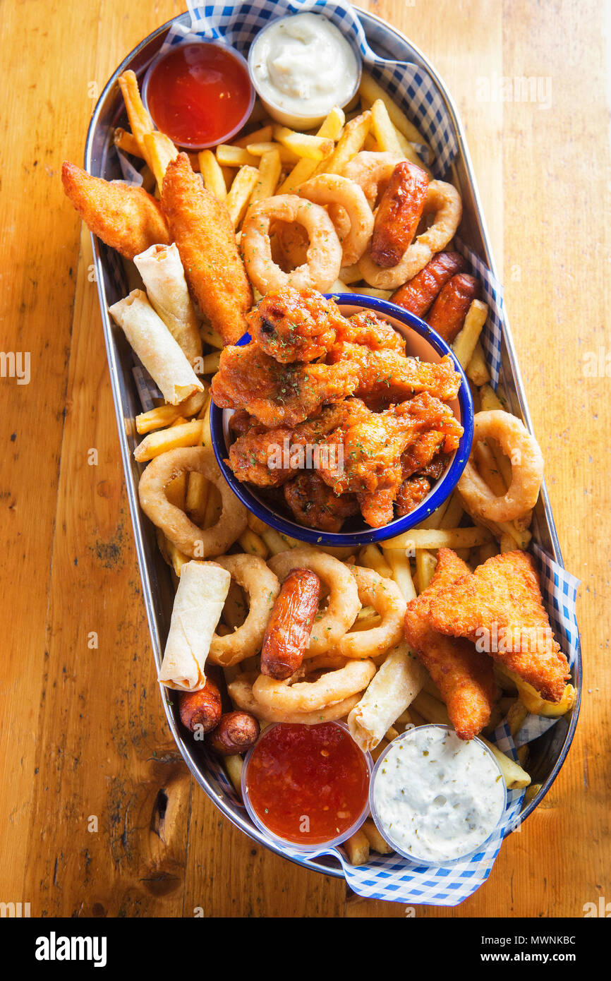 Platter with chicken goujons, crispy chicken wings, cocktail sausages, veg spring rolls, onion rings & fries served with dips Stock Photo