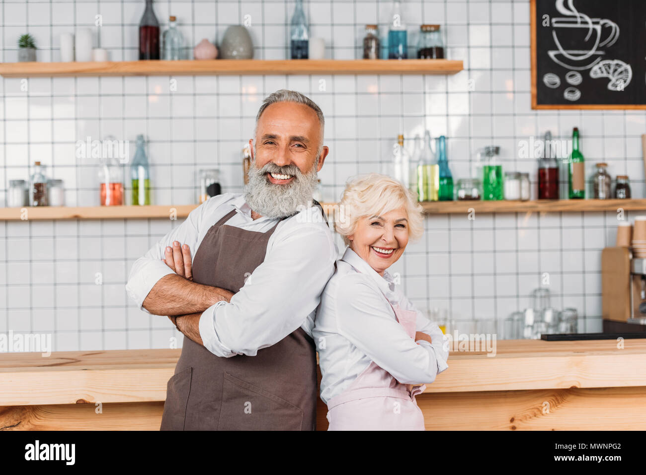 portrait of senior coffee shop owners with arms crossed standing at