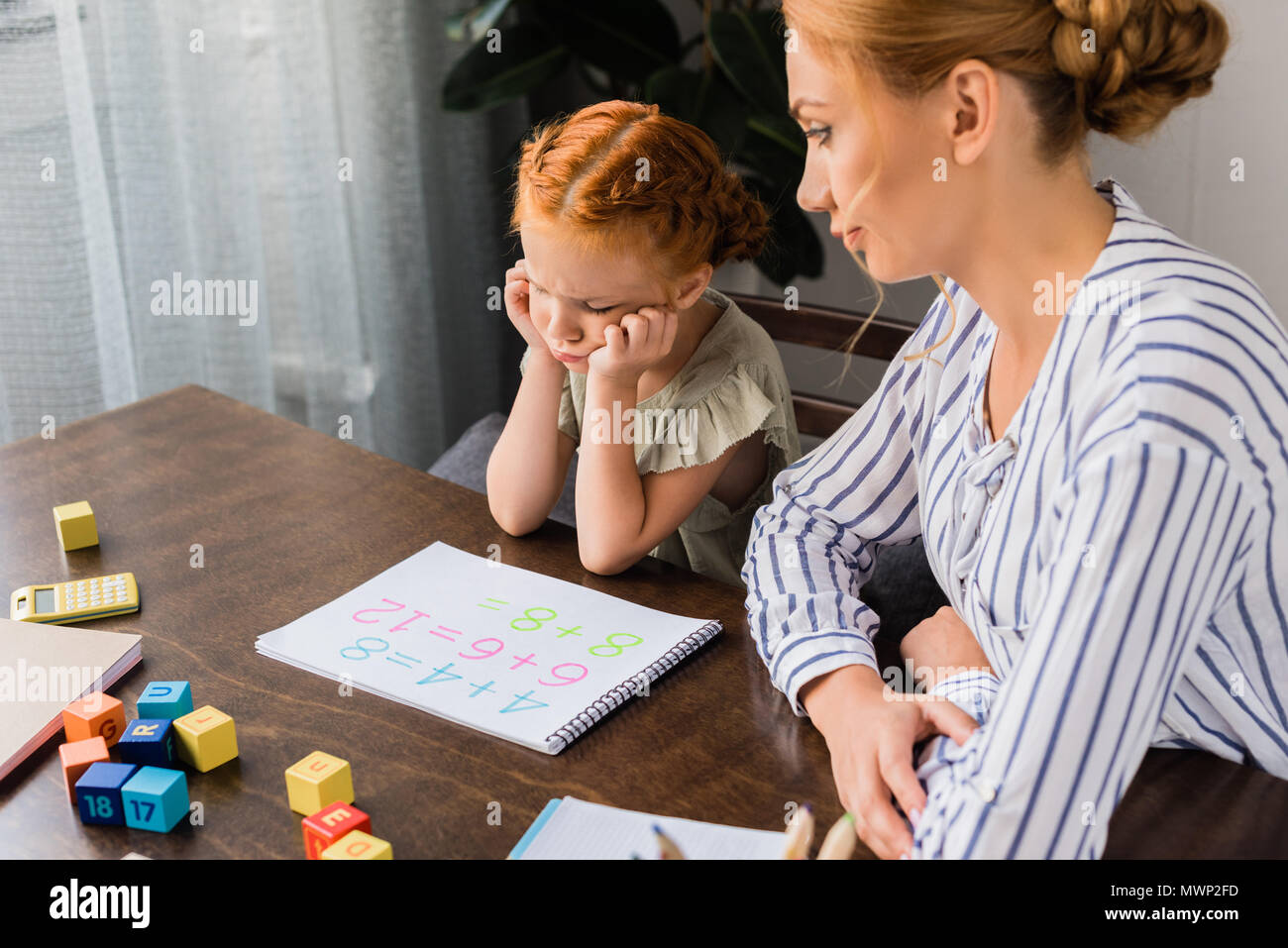 Young mother and depressed daughter learning math at home stock photo