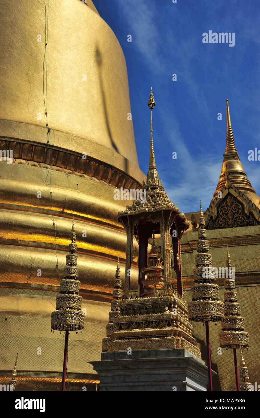 Temple of the Emerald Buddha, gilded tower of the Phra Si Ratana Chedi, with monuments to Chakri kings with multi-tiered umbrellas, Bangkok, Thailand Stock Photo