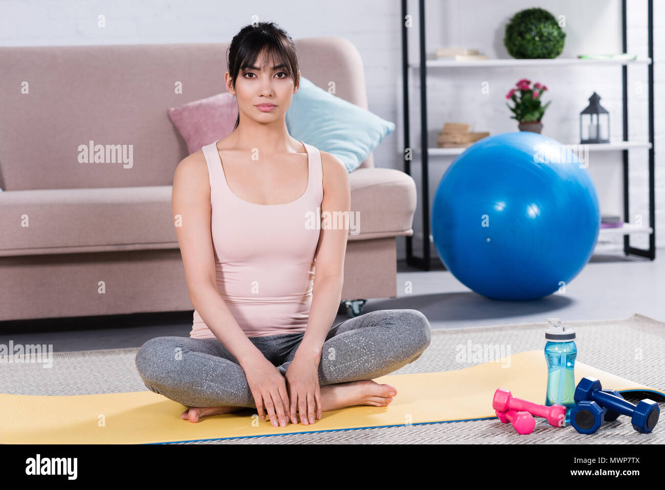 beautiful young woman sitting in relaxed lotus pose on yoga mat at home ...