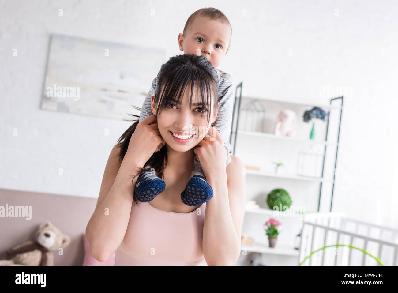 little child riding on shoulders of smiling mother at home Stock Photo