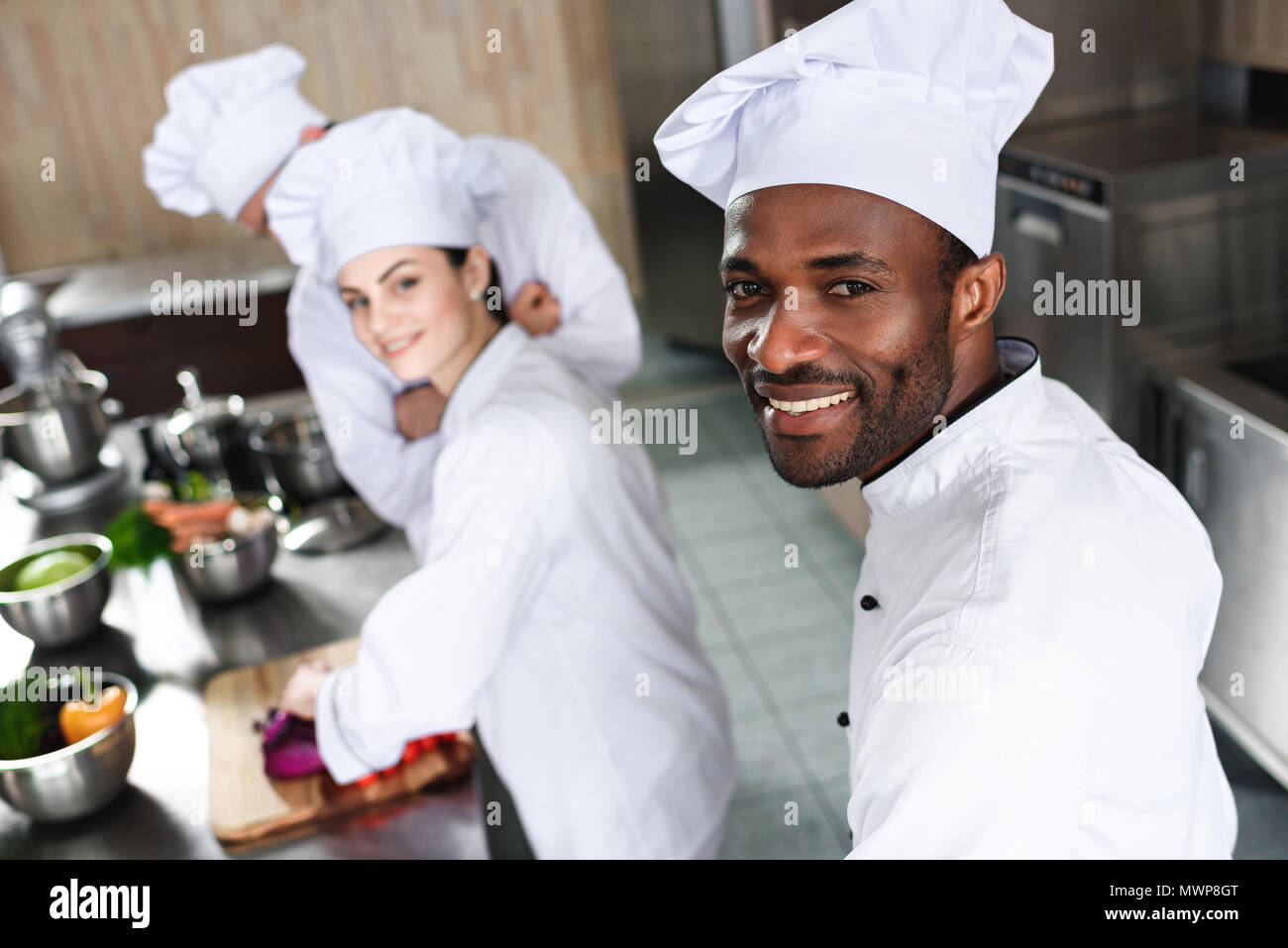 Multiracial chefs team smiling while cooking by kitchen counter Stock Photo