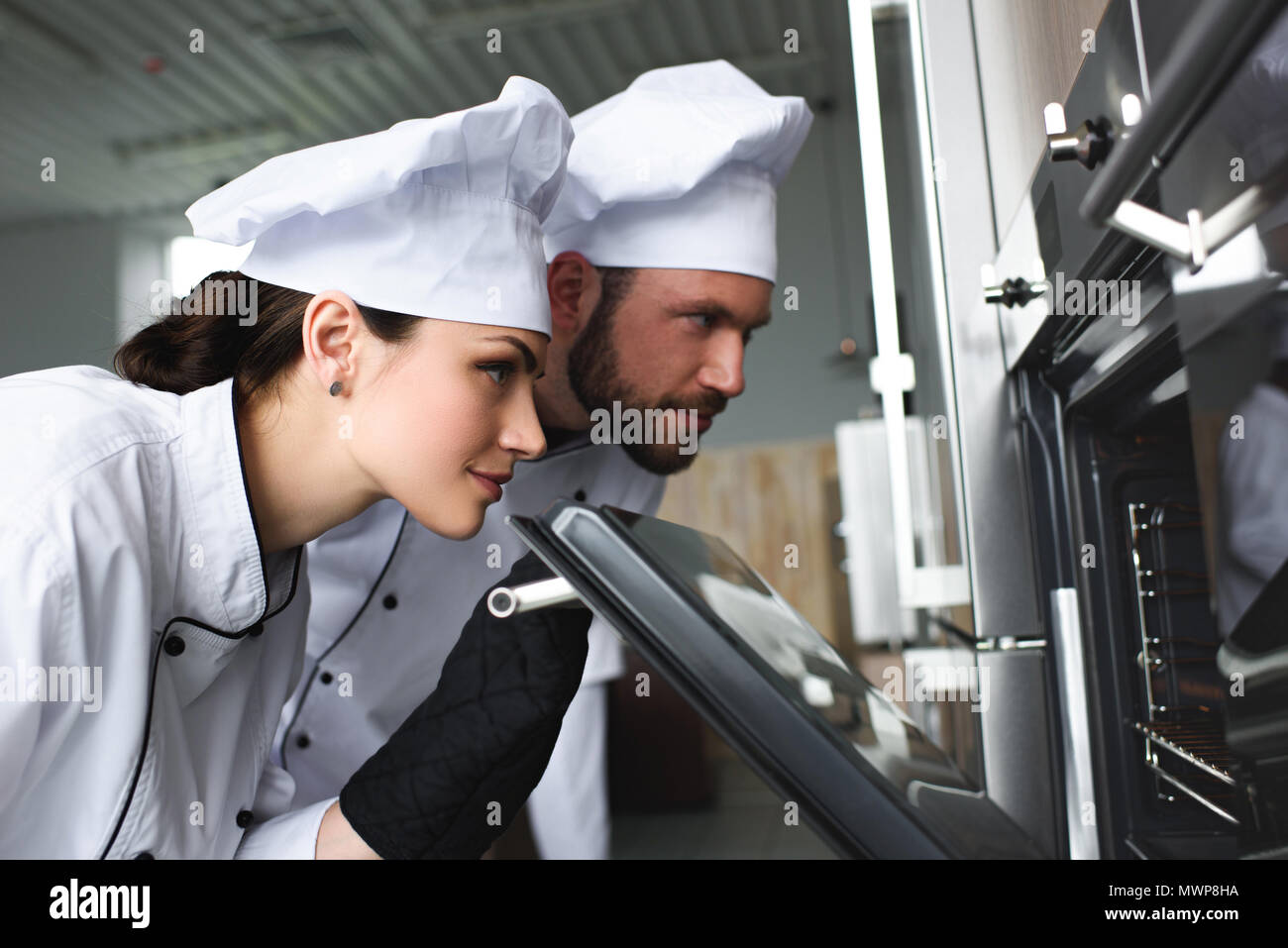 Professional chefs looking into modern kitchen oven Stock Photo