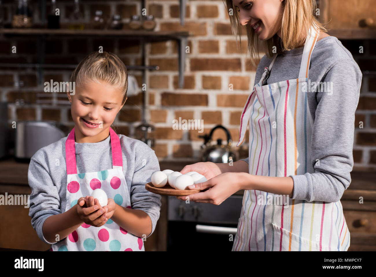 portrait of little girl and mother in aprons holding raw chicken eggs while cooking together Stock Photo