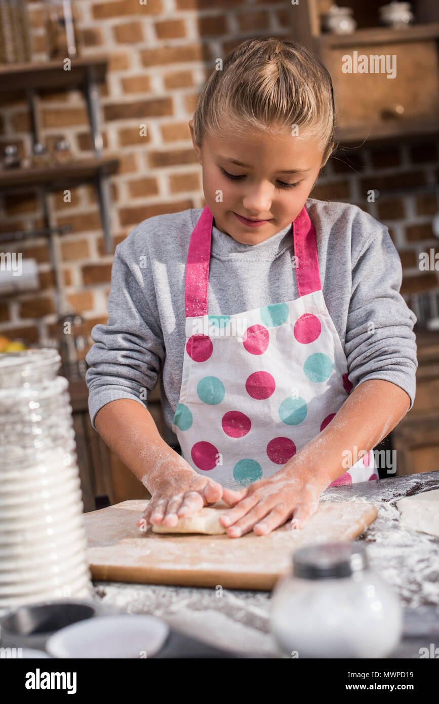 portrait of focused little girl rolling raw dough while cooking at home