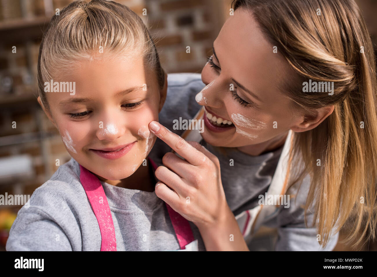 portrait of cheerful mother putting flour on daughters face while