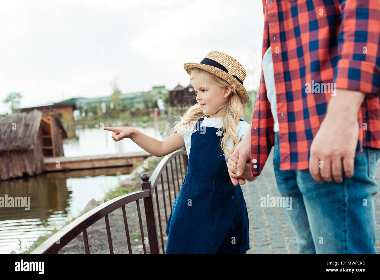 partial view of little girl holding fathers hand and pointing at pond in park Stock Photo