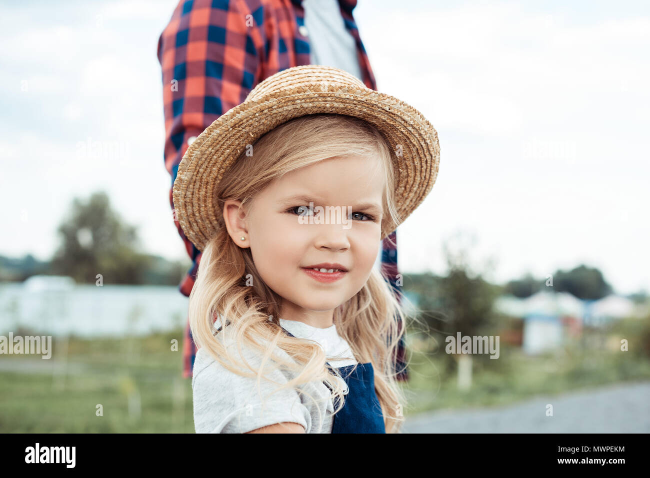 selective focus of cute little girl in straw hat looking at camera ...