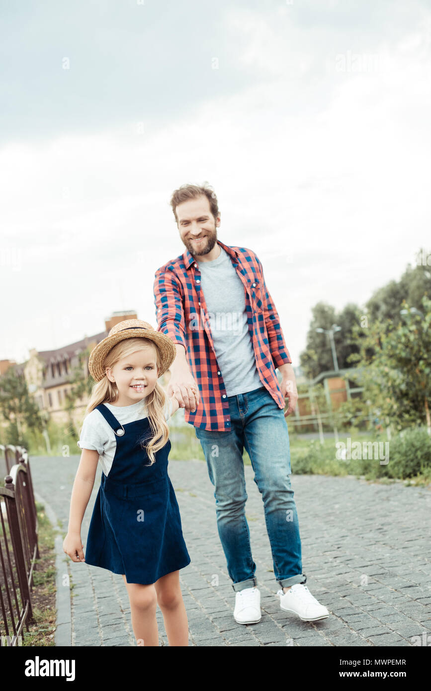 father and little daughter holding hands while walking in park together ...