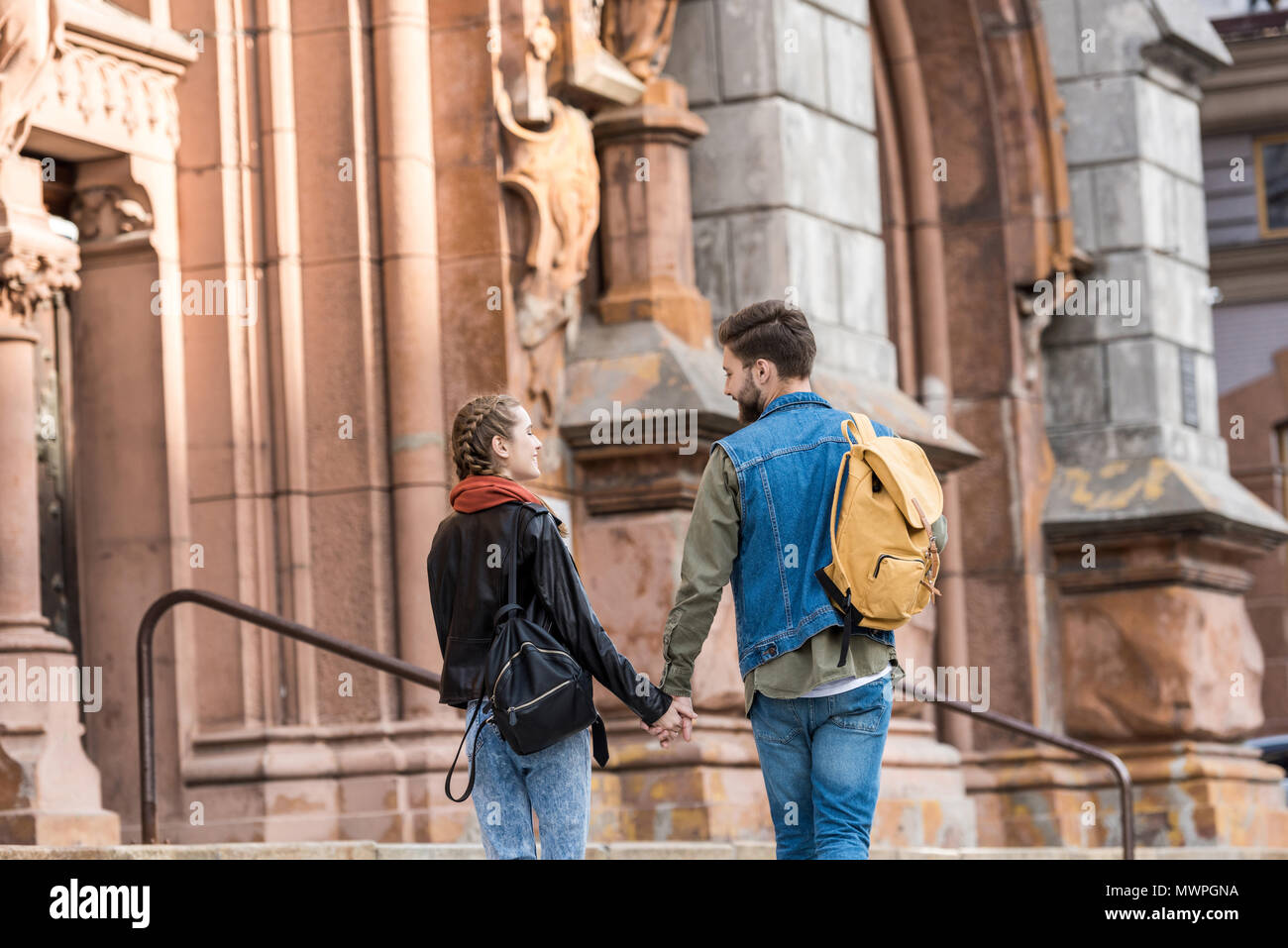 back view of fashionable couple holding hands while walking on street ...