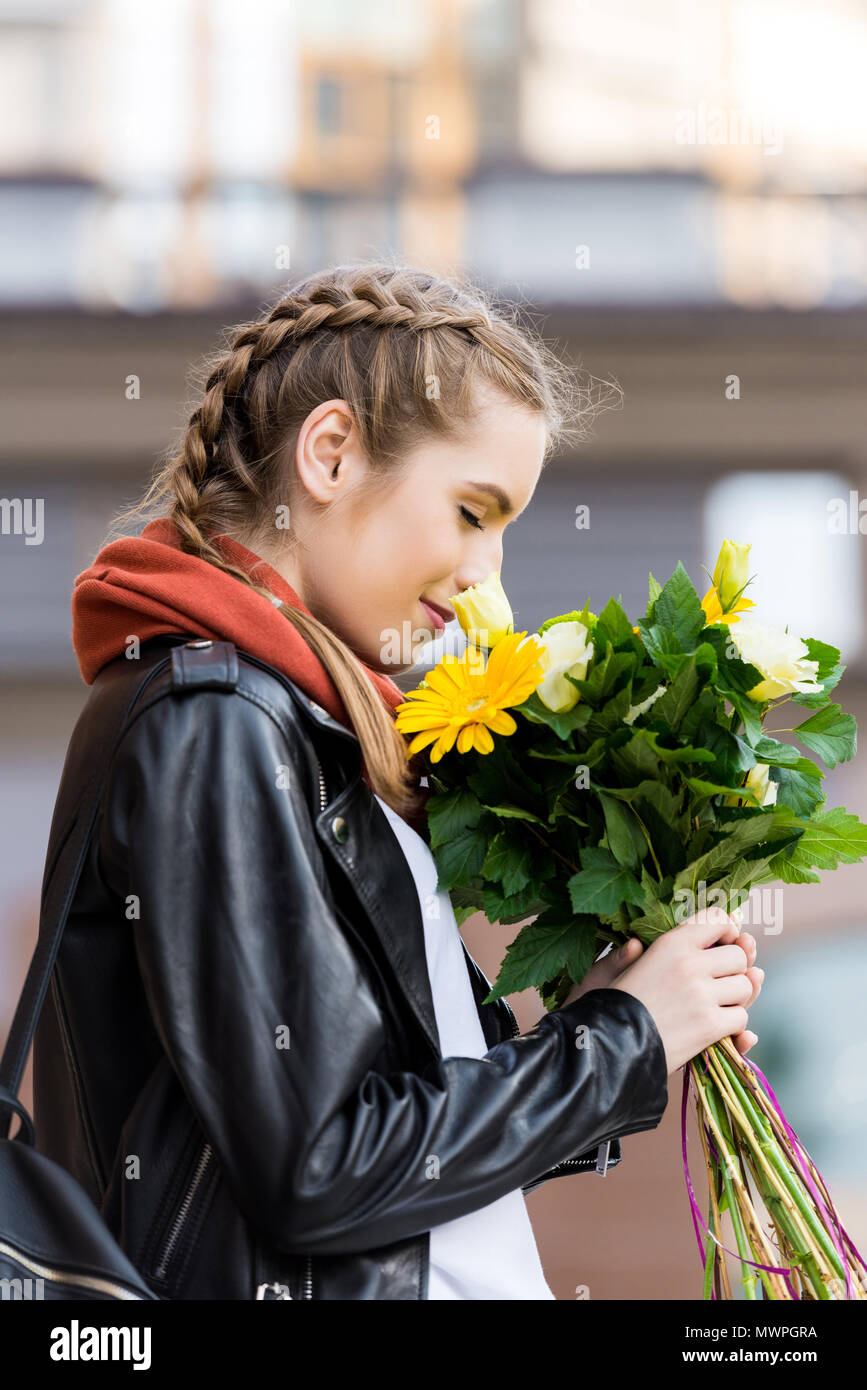 side view of young woman with bouquet of flowers in hands standing on ...