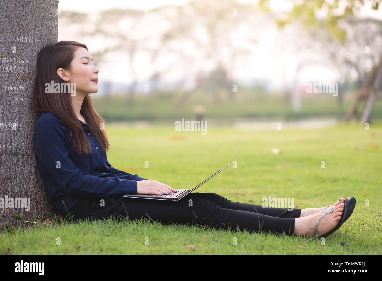Young businesswoman sitting in park working on  notebook. Outdoors work and relaxation concept Stock Photo