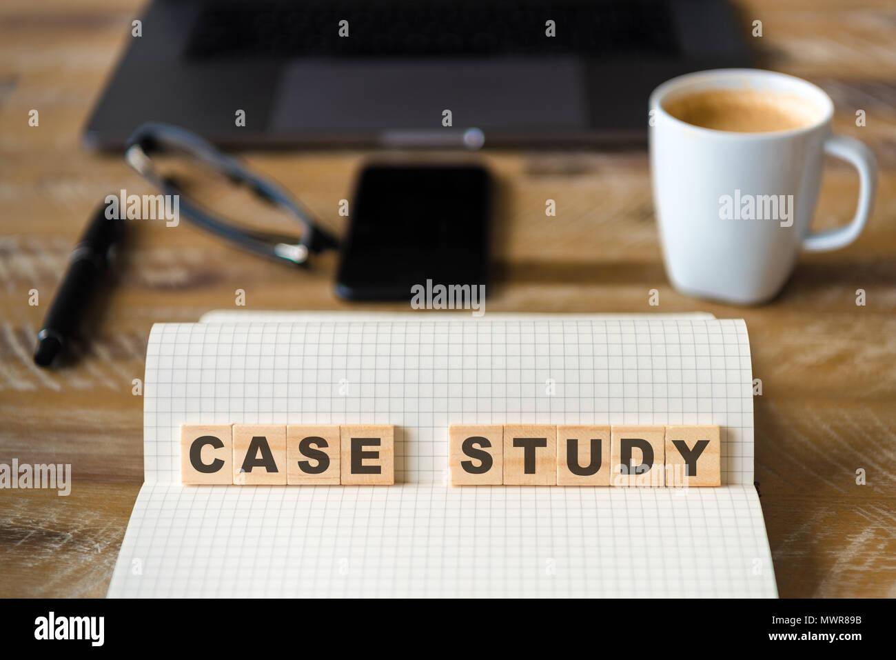 Closeup on notebook over wood table background, focus on wooden blocks with letters making Case Study text. Stock Photo