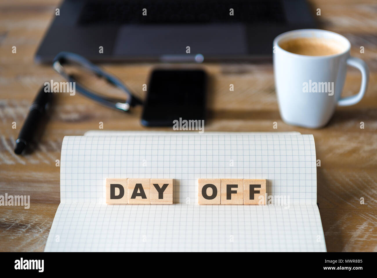 Closeup on notebook over wood table background, focus on wooden blocks with letters making Day Off text. Stock Photo