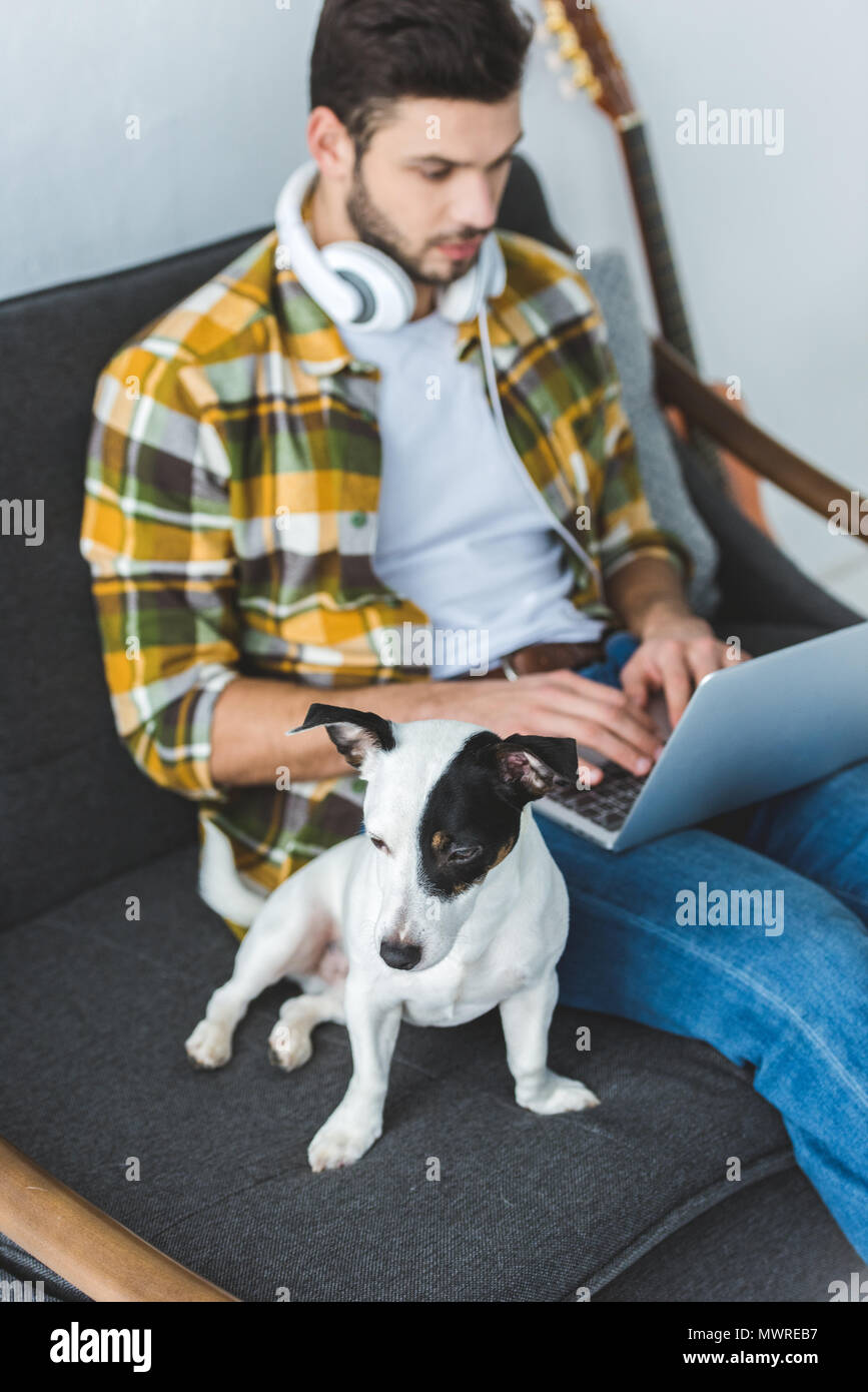 man using laptop while sitting on sofa with jack russell terrier Stock Photo
