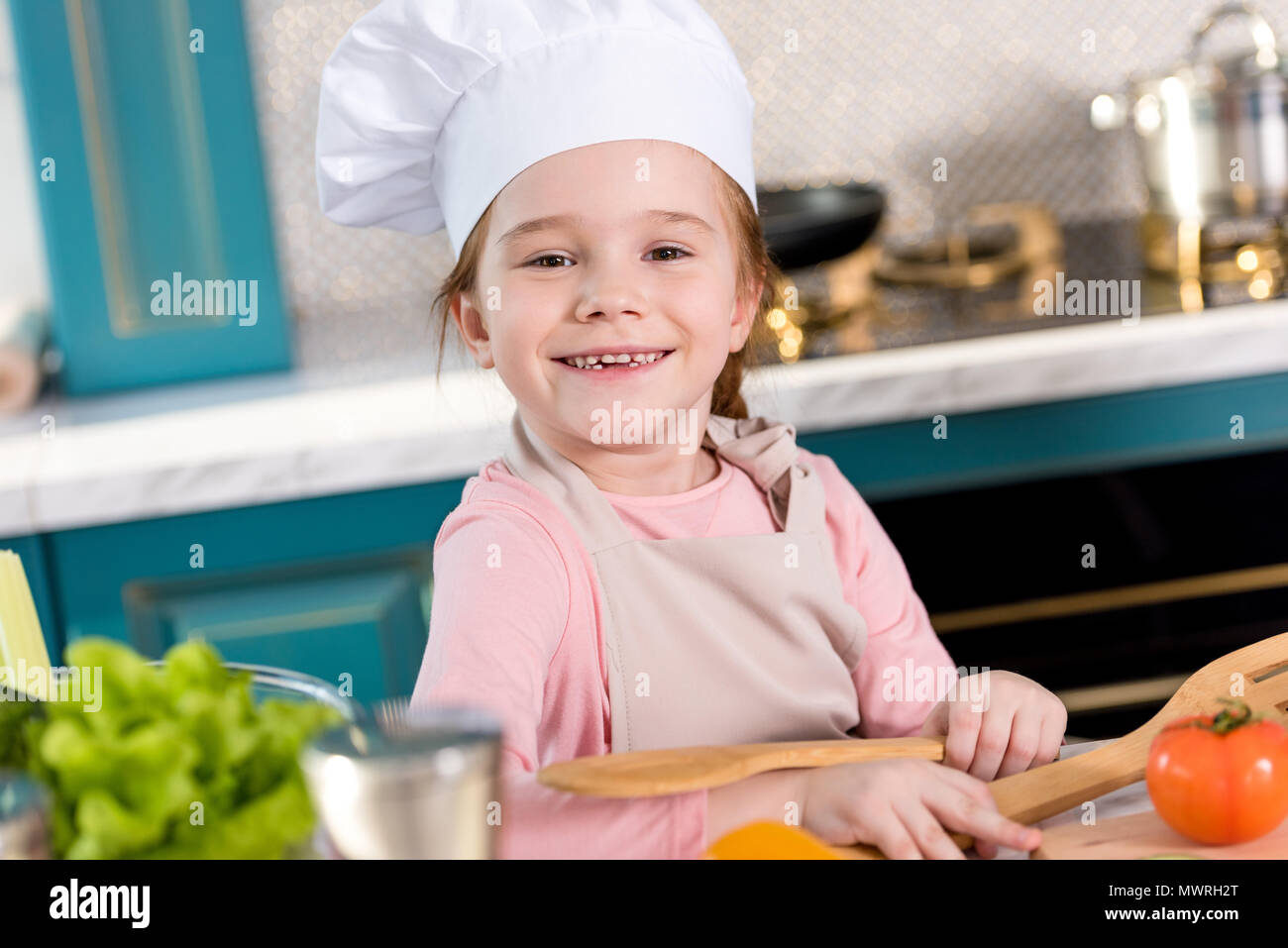 adorable child in chef hat and apron smiling at camera while cooking in kitchen Stock Photo Alamy