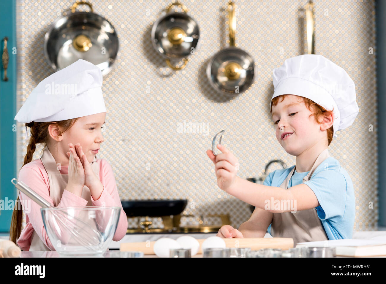 adorable children in chef hats and aprons cooking together in kitchen