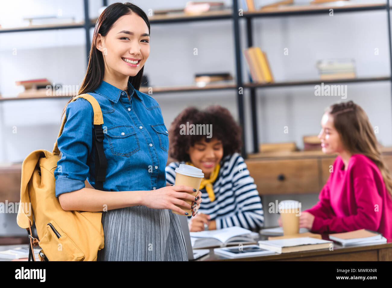 selective focus of smiling asian student with backpack and coffee to go ...
