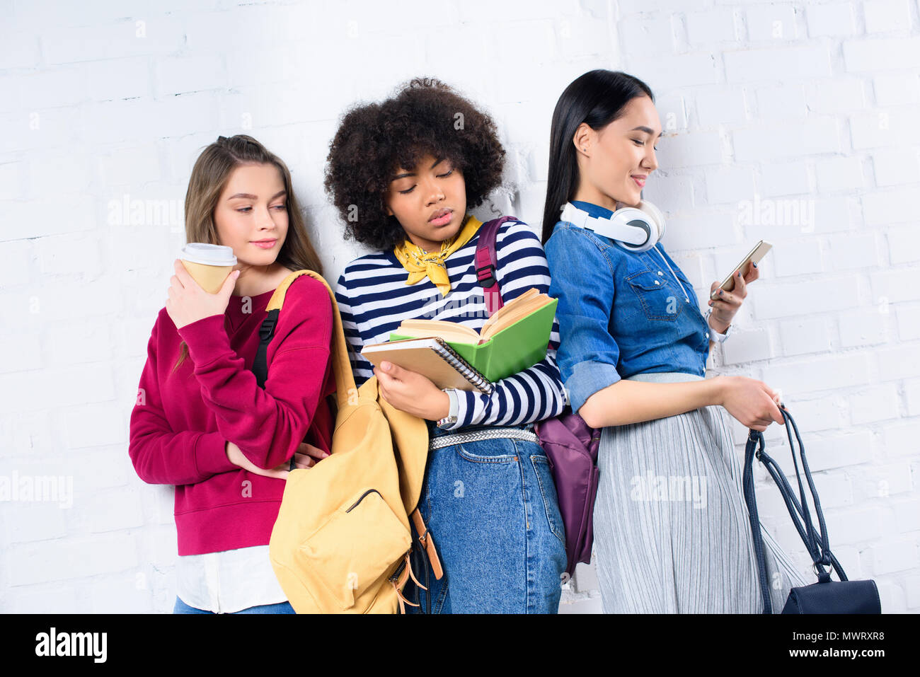 portrait of young multiracial students standing against white brick ...