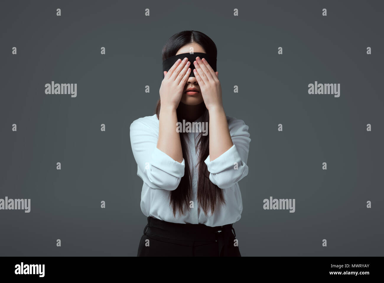 young blindfolded woman closing eyes isolated on grey Stock Photo