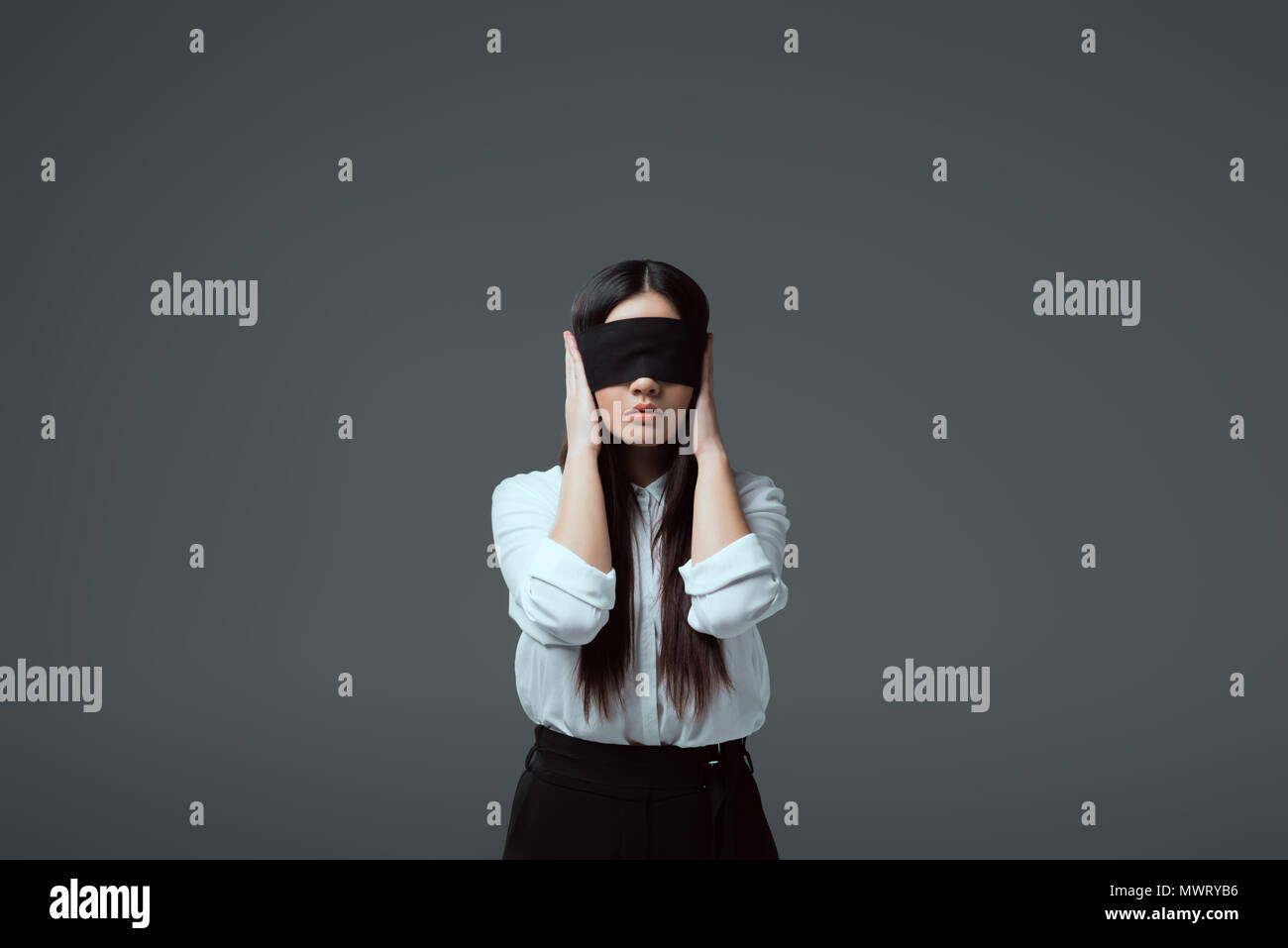 young blindfolded woman closing ears isolated on grey Stock Photo