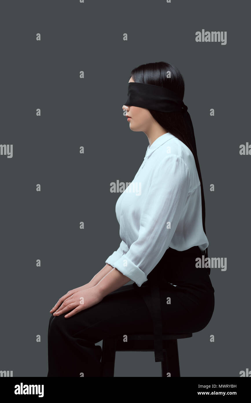 side view of young blindfolded woman sitting on chair isolated on grey Stock Photo