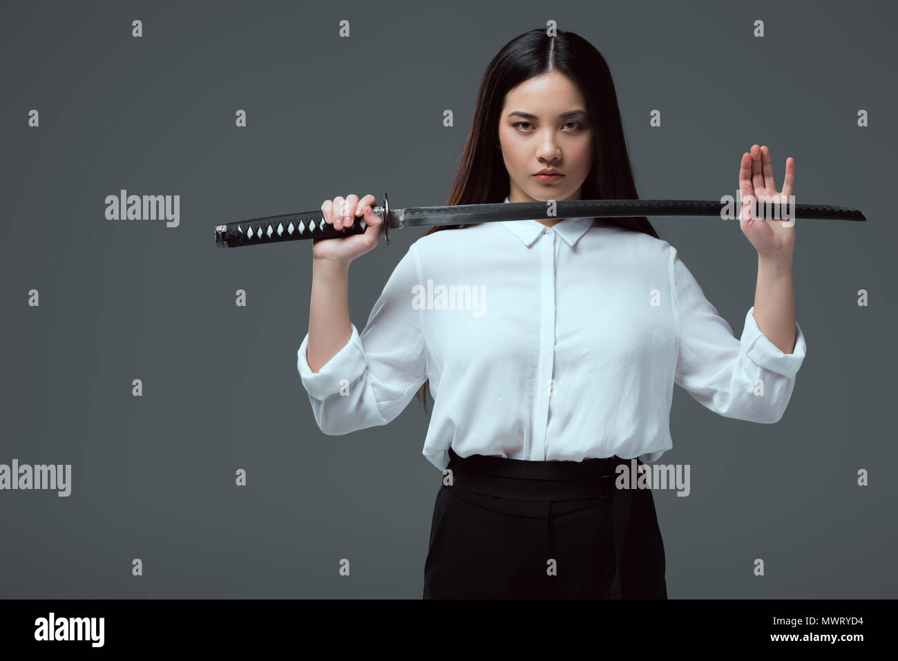 beautiful asian girl holding katana sword and looking at camera isolated on grey Stock - Alamy