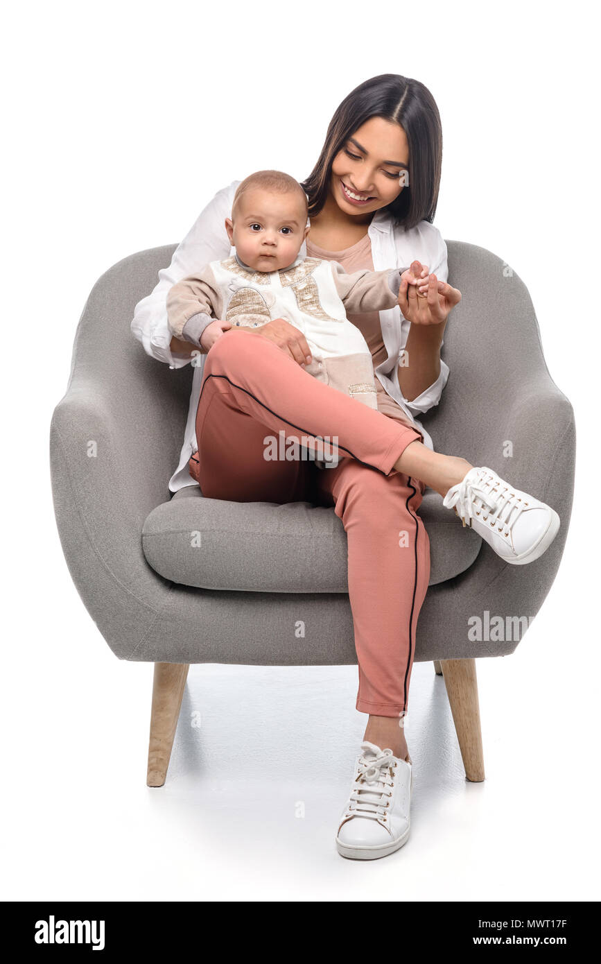 smiling young mother resting on arm chair together with little baby isolated on white Stock Photo