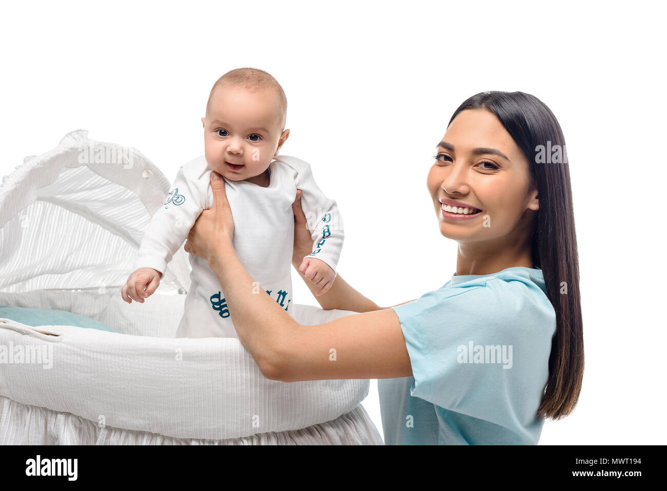 side view of smiling mother taking baby out of crib isolated on white