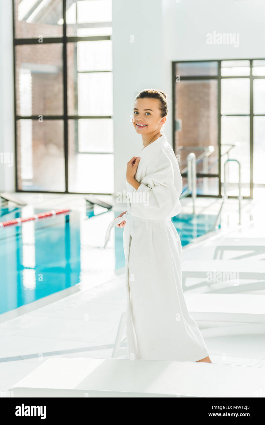 beautiful young woman in bathrobe standing next to swimming pool at spa