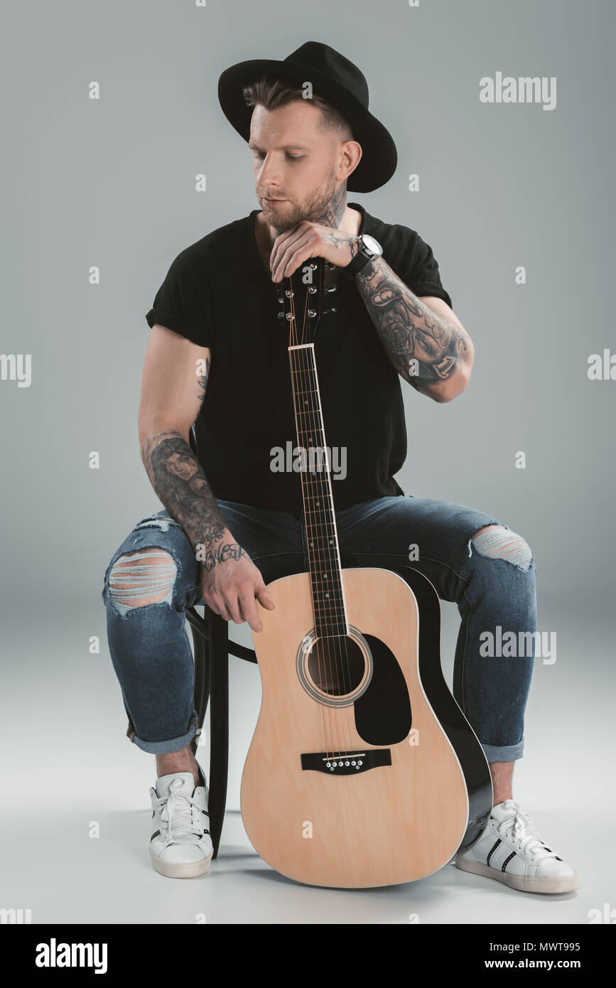 fashionable tattooed guitarist in black hat with acoustic guitar, isolated  on grey Stock Photo - Alamy