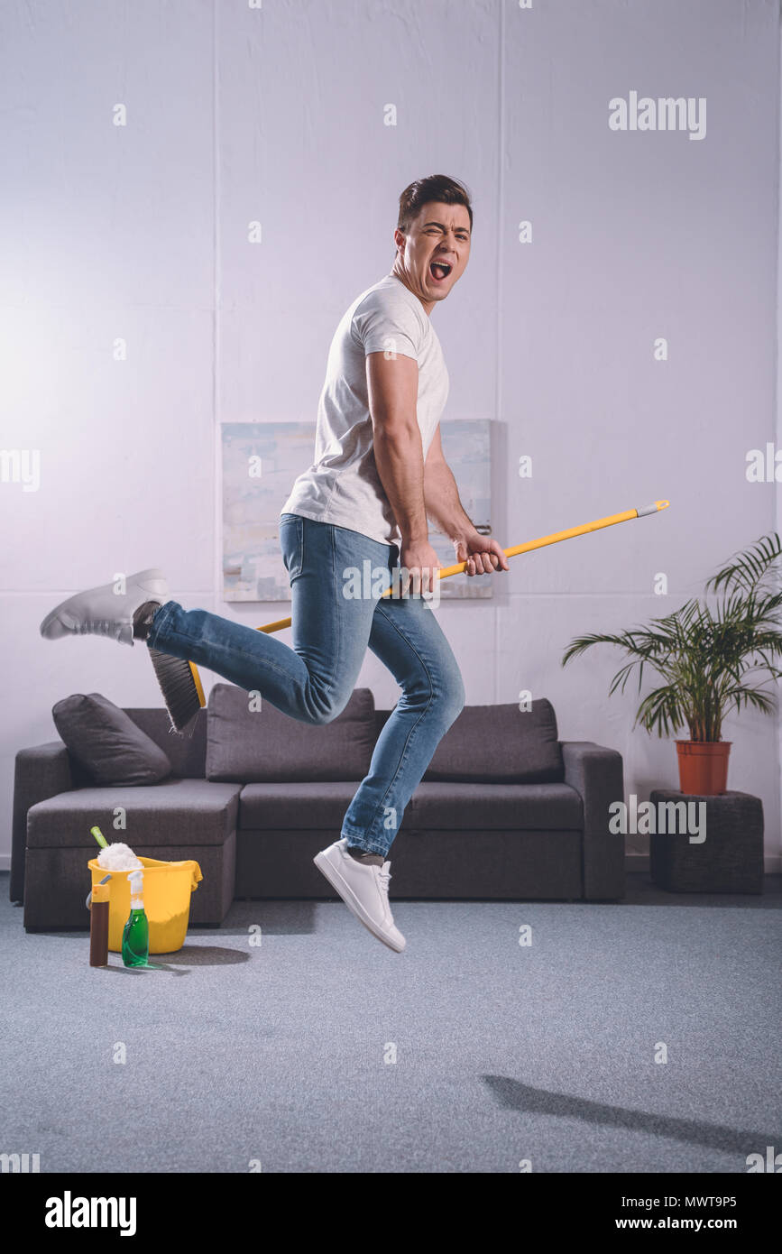 handsome man jumping with broom in living room Stock Photo