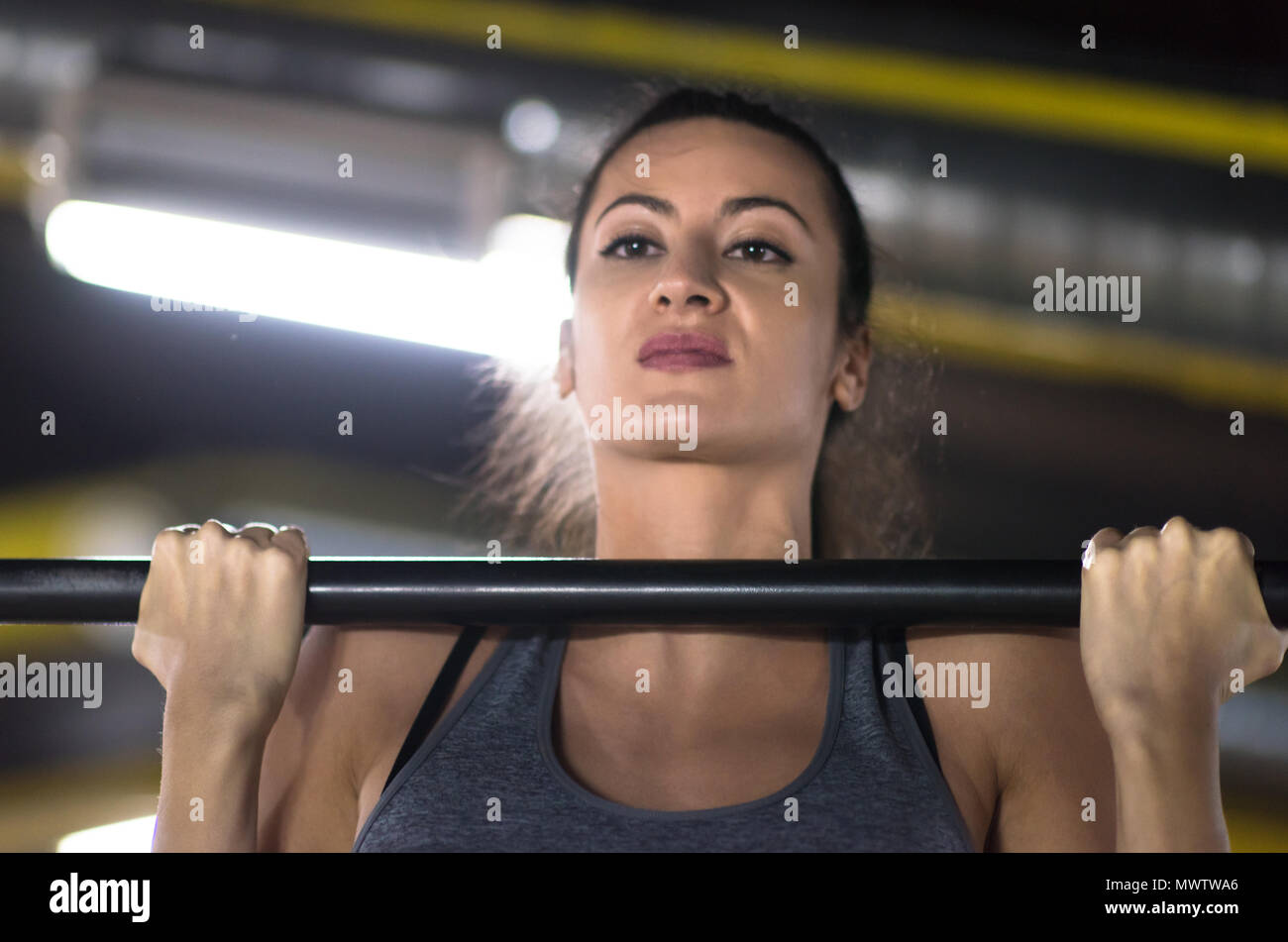 young muscular woman doing pull ups on the horizontal bar as part of ...