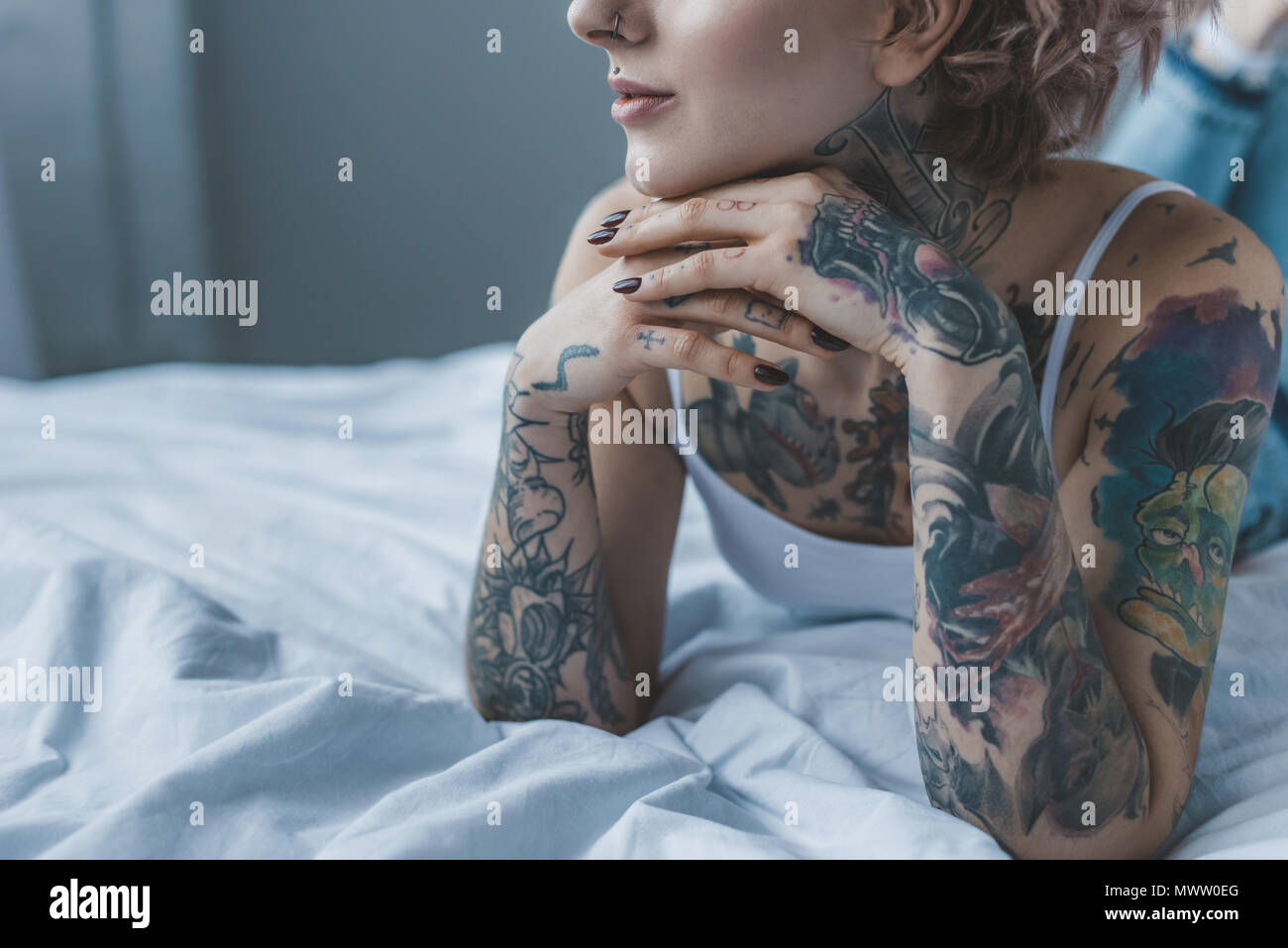 cropped view of dreamy tattooed girl lying on bed Stock Photo